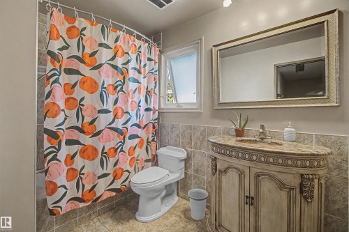 Bathroom featuring a curved shower rod, a white toilet, a decorative vanity with an integrated sink and stone countertop, a framed mirror, and a window with privacy glass - 11617 26 Avenue, Edmonton, AB - Indoor Photo Showing Bathroom