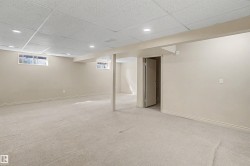 Spacious lower-level room featuring light-toned carpeting, neutral wall paint, and a drop ceiling with recessed lighting - 