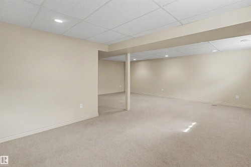 Expansive finished basement featuring neutral carpeting, light beige wall finishes, a drop ceiling with recessed lighting, and a structural beam - 11617 26 Avenue, Edmonton, AB - Indoor