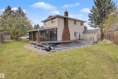 Rear exterior featuring a sunroom addition, brick chimney, and a covered in-ground pool - 11617 26 Avenue, Edmonton, AB - Outdoor