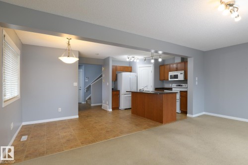 Open concept living space featuring a kitchen island with built-in sink, wood-finish cabinetry, and a full suite of white appliances - 9071 Scott Crescent, Edmonton, AB - Indoor Photo Showing Kitchen