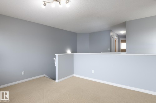 Carpeted landing area featuring track lighting, light grey walls, white trim, and a partial wall with a white banister - 9071 Scott Crescent, Edmonton, AB - Indoor Photo Showing Other Room