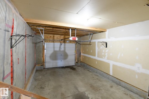Single-bay garage with a concrete floor, an overhead door with opener mechanism, exposed ceiling joists, and partially finished walls - 9071 Scott Crescent, Edmonton, AB - Indoor Photo Showing Garage