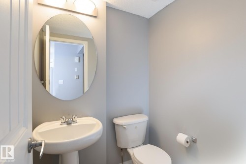 Pedestal sink with chrome fixtures, oval mirror, and overhead vanity lighting - 9071 Scott Crescent, Edmonton, AB - Indoor Photo Showing Bathroom
