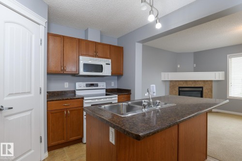 Kitchen featuring medium wood-finish cabinetry, dark speckled countertops, and a double basin stainless steel sink - 9071 Scott Crescent, Edmonton, AB - Indoor Photo Showing Kitchen With Fireplace With Double Sink