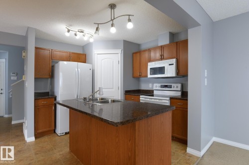 Kitchen featuring wood-finish cabinetry, dark speckled countertops, and a central island with an integrated double basin sink - 9071 Scott Crescent, Edmonton, AB - Indoor Photo Showing Kitchen With Double Sink