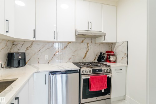 Modern kitchen featuring white cabinetry, a stainless steel range, and a patterned backsplash - 219 28 Street, Edmonton, AB - Indoor Photo Showing Kitchen