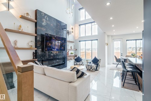 Bright living area featuring high ceilings, large windows, a dark stone-finish fireplace, built-in shelving, and polished tile flooring - 219 28 Street, Edmonton, AB - Indoor Photo Showing Living Room With Fireplace