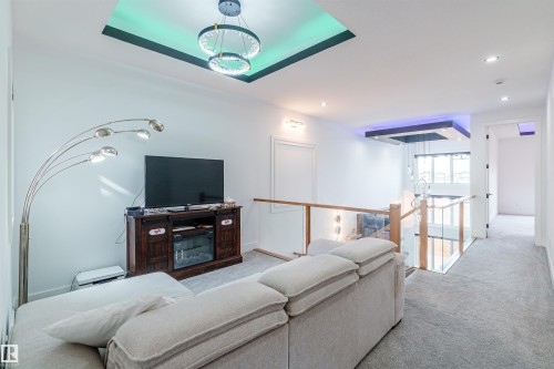 Loft space featuring recessed ceiling with accent lighting, contemporary chandelier, glass railing, and light gray carpet - 219 28 Street, Edmonton, AB - Indoor
