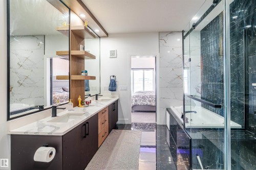 Bathroom featuring a dual vanity with white countertops and black cabinetry, wood-finish shelving, a large framed mirror, and a glass-enclosed shower with dark tile accents - 219 28 Street, Edmonton, AB - Indoor Photo Showing Bathroom