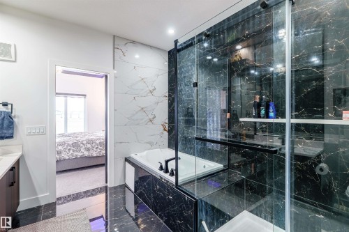 Bathroom featuring a soaking tub with black fixtures, dark stone-finish wall and floor tiles, a glass-enclosed shower, and a white wall with light stone-finish accents - 219 28 Street, Edmonton, AB - Indoor Photo Showing Bathroom