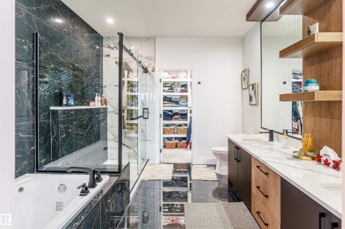 Contemporary bathroom featuring a deep soaking tub with a black faucet, a glass-enclosed shower with black-veined wall tile, and a dual vanity with a white countertop and wood-finish cabinetry - 219 28 Street, Edmonton, AB - Indoor Photo Showing Bathroom