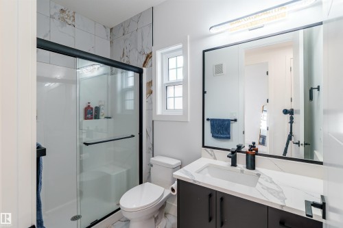 Full bathroom featuring a shower with black-framed glass doors, a white vanity with a rectangular sink and marble-look countertop, black-finish fixtures, and a window with grid detailing - 219 28 Street, Edmonton, AB - Indoor Photo Showing Bathroom