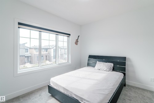 Room featuring a large multi-pane window with a roller shade, light gray wall-to-wall carpeting, white painted walls, and white baseboards - 219 28 Street, Edmonton, AB - Indoor Photo Showing Bedroom