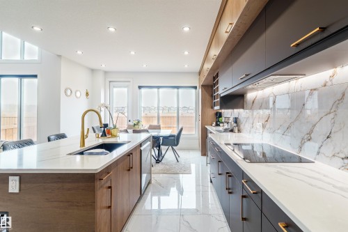 Modern kitchen featuring a large island with an undermount sink and golden faucet, integrated dishwasher, and wood-finish cabinetry - 219 28 Street, Edmonton, AB - Indoor Photo Showing Kitchen With Double Sink With Upgraded Kitchen