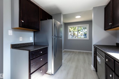 Kitchen featuring dark wood cabinetry, stainless steel refrigerator and dishwasher, dark speckled countertops, and wood-finish flooring - 547 Dunluce Road, Edmonton, AB - Indoor Photo Showing Kitchen