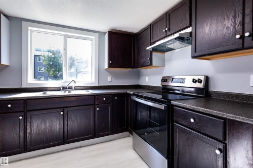 Kitchen featuring dark wood-finish cabinetry, a stainless steel range with overhead hood, and a dual basin sink beneath a large window - 547 Dunluce Road, Edmonton, AB - Indoor Photo Showing Kitchen With Double Sink