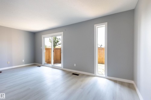 Spacious interior featuring light-toned wood-finish flooring, a sliding glass door, and an elongated vertical window - 547 Dunluce Road, Edmonton, AB - Indoor Photo Showing Other Room