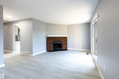 Living room featuring a brick fireplace with a white mantle, light wood-finish flooring, and a sliding glass door - 547 Dunluce Road, Edmonton, AB - Indoor Photo Showing Living Room With Fireplace