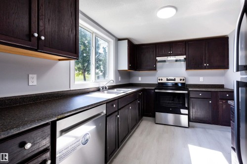 Kitchen featuring dark wood cabinetry, solid surface countertops, stainless steel appliances, a double basin sink, and light wood-finish flooring - 547 Dunluce Road, Edmonton, AB - Indoor Photo Showing Kitchen With Double Sink