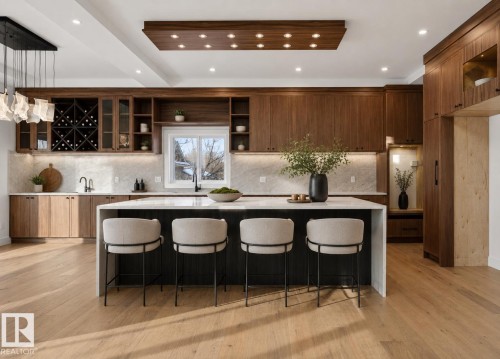Gourmet kitchen featuring a waterfall island with integrated seating, extensive wood-finish cabinetry, a built-in wine rack, light wood-finish flooring, and a recessed ceiling panel with integrated lighting - 5820 110 Street, Edmonton, AB - Indoor Photo Showing Kitchen With Upgraded Kitchen