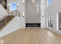Two-story living area featuring a full-height tiled fireplace, light wood-finish flooring, a contemporary wood and metal railing staircase, and large windows - 