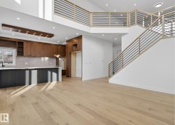 Open-concept living area featuring light wood-finish flooring, a two-story ceiling, and a contemporary staircase with wood and metal railings - 