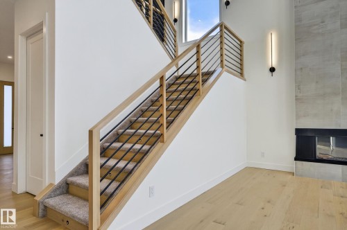 Modern staircase featuring wood railings, black metal balusters, and carpeted treads - 5820 110 Street, Edmonton, AB - Indoor Photo Showing Other Room With Fireplace