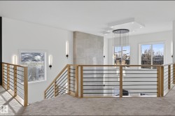 Open-concept upper-level featuring light wood and black metal railings, a textured accent wall, recessed lighting, and a multi-tiered chandelier - 