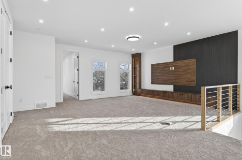 Spacious carpeted room featuring recessed lighting, multiple windows, a built-in media center with wood-finish cabinetry and shelving, and a contemporary railing system with metal balusters - 5820 110 Street, Edmonton, AB - Indoor Photo Showing Other Room