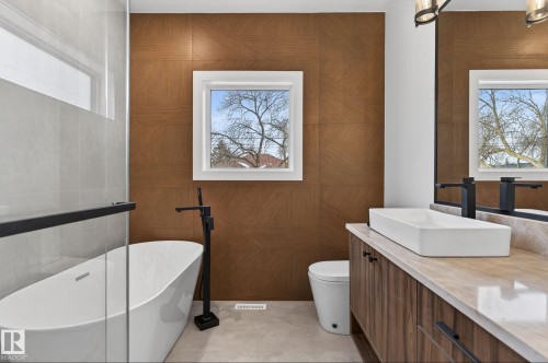 Modern bathroom featuring a freestanding tub with a matte black floor-mounted faucet, a rectangular vessel sink set on a light-colored countertop, and wood-finish cabinetry - 5820 110 Street, Edmonton, AB - Indoor Photo Showing Bathroom
