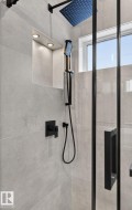 Shower featuring large format light gray wall tiles, a black framed glass enclosure, and a square rain shower head with matching handheld wand - 