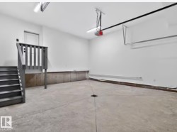 Spacious garage featuring a concrete floor, painted walls, overhead lighting, and a finished staircase with handrails providing interior access - 