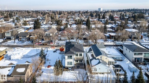 Modern multi-story property with a dark-pitched roof and light-colored siding, situated in a residential area featuring established tree cover - 5820 110 Street, Edmonton, AB - Outdoor With View