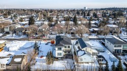 Modern multi-story property with a dark-pitched roof and light-colored siding, situated in a residential area featuring established tree cover - 