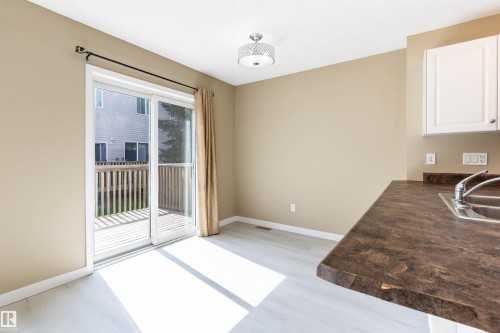Sliding glass patio door opening to an outdoor deck featuring wood-finish flooring, a stainless steel double-basin sink, and white upper cabinetry - #116 5001 62 St, Beaumont, AB - Indoor