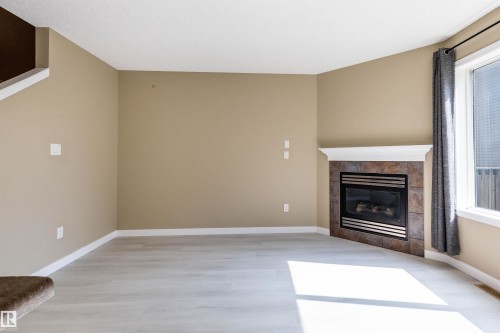 Living space featuring light wood-finish flooring, neutral-toned walls, and white baseboards - #116 5001 62 St, Beaumont, AB - Indoor Photo Showing Living Room With Fireplace