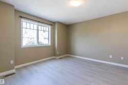 Spacious room featuring light wood-finish flooring, neutral wall tones, white baseboards, and a large window with divided lites and a black decorative curtain rod - 