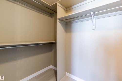 Corner closet featuring shelving and clothes hanging rods, wood-finish flooring, and light-toned walls - #116 5001 62 St, Beaumont, AB - Indoor With Storage