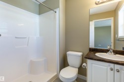 Bathroom featuring a white shower stall with a built-in seat, a single vanity with a dark countertop and undermount sink, a chrome faucet, and a toilet - 