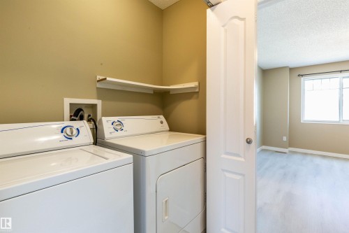 Dedicated laundry area featuring a washer and dryer, an overhead corner shelf, and neutral wall paint - #116 5001 62 St, Beaumont, AB - Indoor Photo Showing Laundry Room