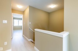 Hallway with light wood-finish flooring, neutral-toned walls, white baseboards, and a modern ceiling light fixture - 