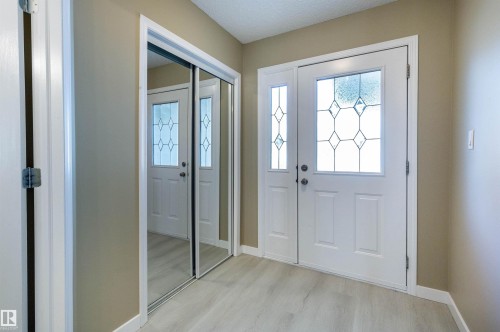 Entryway featuring a white paneled door with decorative glass inserts, a coordinating sidelight, light wood-finish flooring, and a mirrored closet door - #116 5001 62 St, Beaumont, AB - Indoor Photo Showing Other Room