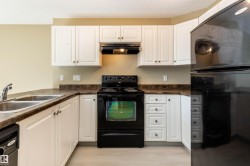 Kitchen featuring white cabinetry, dark countertops, a black electric range, a double basin stainless steel sink, and light wood-finish flooring - 