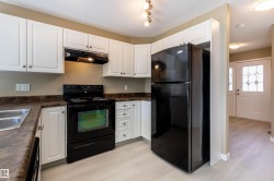 Kitchen featuring white cabinetry with brushed nickel hardware, dark countertop surfaces, black electric range with overhead ventilation, and a black refrigerator - 