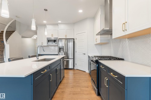 Modern kitchen featuring an island with an undermount sink, quartz countertops, stainless steel appliances, and a tiled backsplash - 6003 Edmonds Place Nw, Edmonton, AB - Indoor Photo Showing Kitchen With Double Sink With Upgraded Kitchen