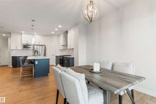 Modern kitchen and dining area featuring wood-finish flooring, a kitchen island with seating, stainless steel appliances, white subway tile backsplash, and recessed lighting - 6003 Edmonds Place Nw, Edmonton, AB - Indoor Photo Showing Dining Room