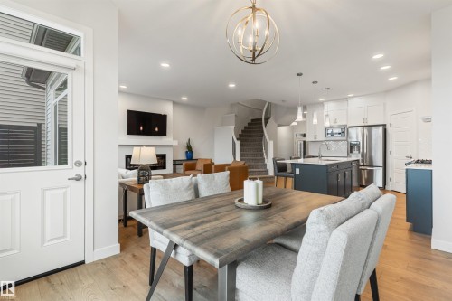 Open-concept living space featuring wood-finish flooring, a contemporary kitchen with stainless steel appliances and a center island, and a fireplace with a mantel - 6003 Edmonds Place Nw, Edmonton, AB - Indoor Photo Showing Dining Room