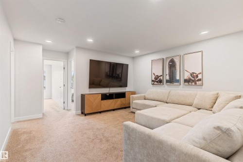 Spacious entertainment area with neutral-toned carpeting, recessed lighting, and a modern media console - 6003 Edmonds Place Nw, Edmonton, AB - Indoor Photo Showing Living Room