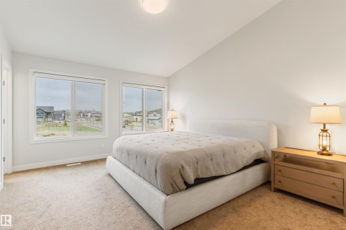 Spacious bedroom featuring multiple windows, neutral wall tones, light-toned carpeting, and a built-in overhead light fixture - 6003 Edmonds Place Nw, Edmonton, AB - Indoor Photo Showing Bedroom